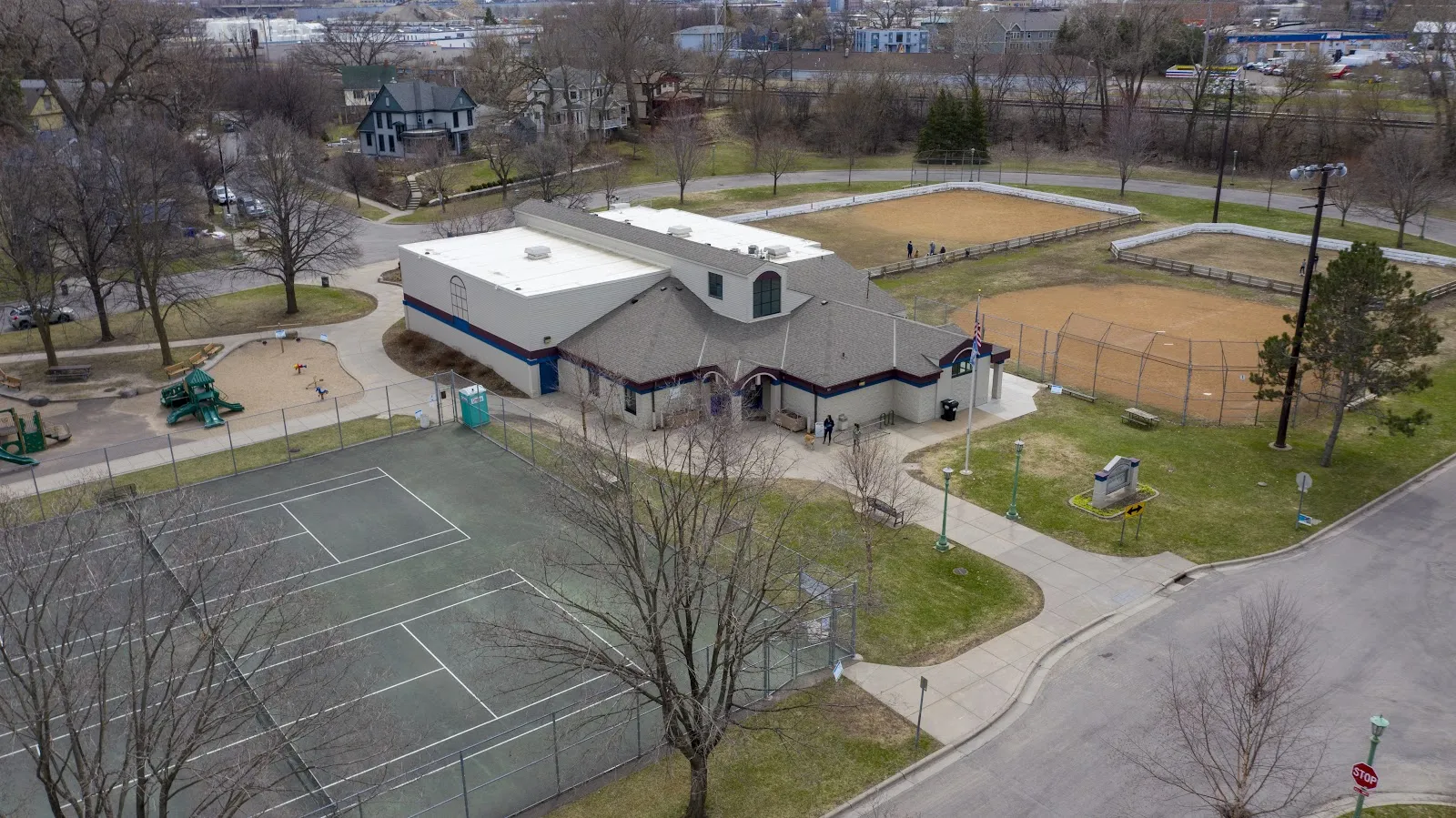 An aerial view of the Langford Park Recreation Center, the warming-house building beside the outdoor rinks, with tennis courts and ball diamonds around it. — Langford Park Outdoor Rinks