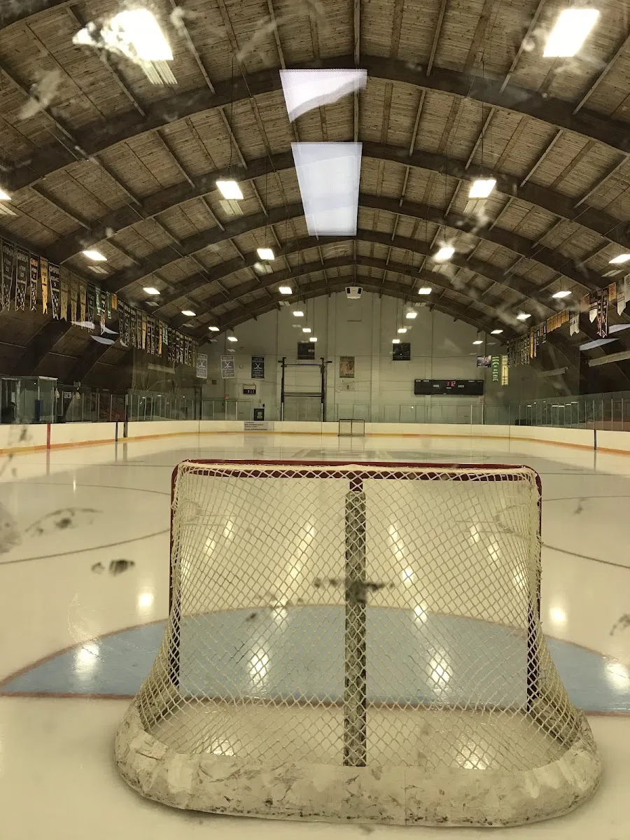 The Langton arena ice from behind a net, under the curved wooden barrel roof with championship banners along the walls. — Langton Arena