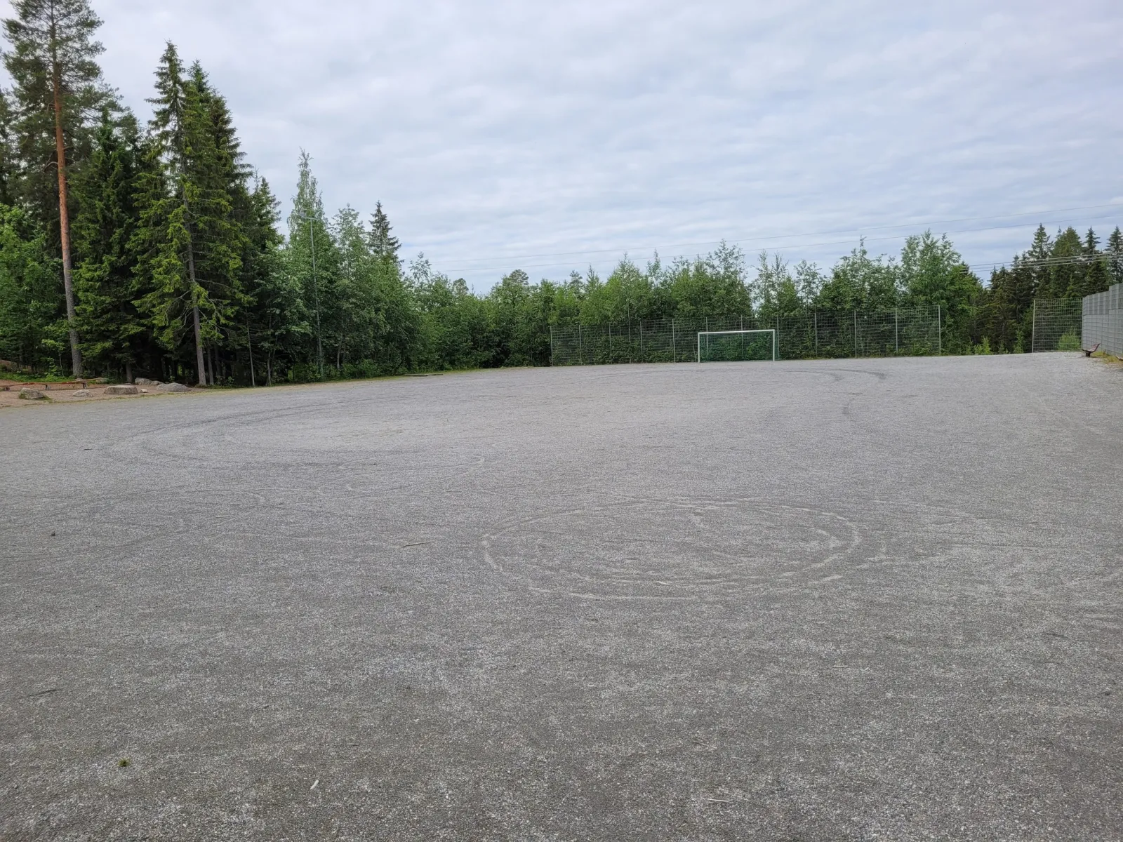 The gravel field at Länsi-Puijo in Kuopio, which serves as a skating field in winter, seen in summer with a goal at the far end and spruces behind. — Länsi-Puijon luistelukenttä