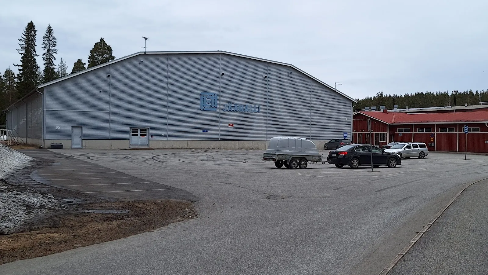 The grey steel-clad Lapinlahti ice hall seen across its car park with a flagpole beside it. — Lapinlahden jäähalli