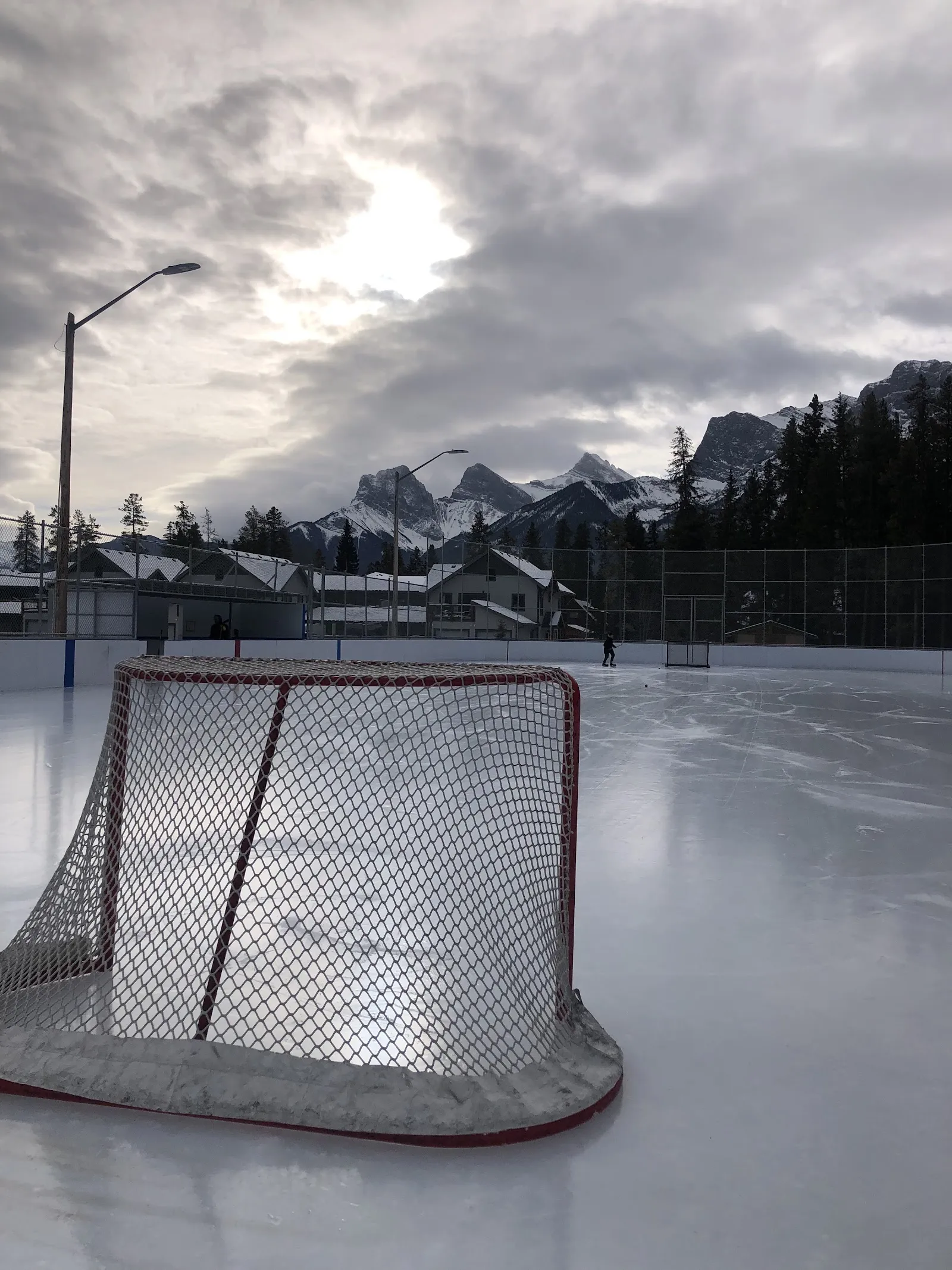 The boarded Larch rink in Canmore with a hockey goal on the ice and the mountains behind. — Larch Boarded Ice Rink