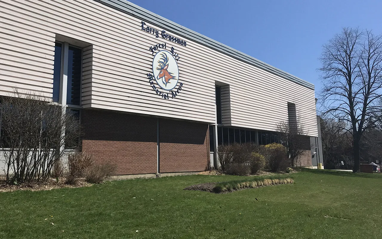 The side of the Larry Grossman Forest Hill Memorial Arena with the arena crest on its wall, beyond a lawn and bare trees. — Larry Grossman Forest Hill Memorial Arena