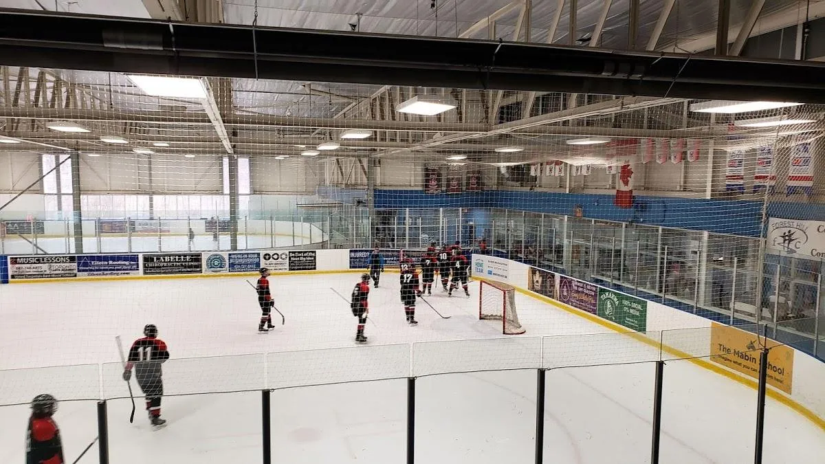 The ice at the Larry Grossman Forest Hill Memorial Arena with a youth hockey session at the far end, sponsor boards along the glass and a steel roof overhead. — Larry Grossman Forest Hill Memorial Arena