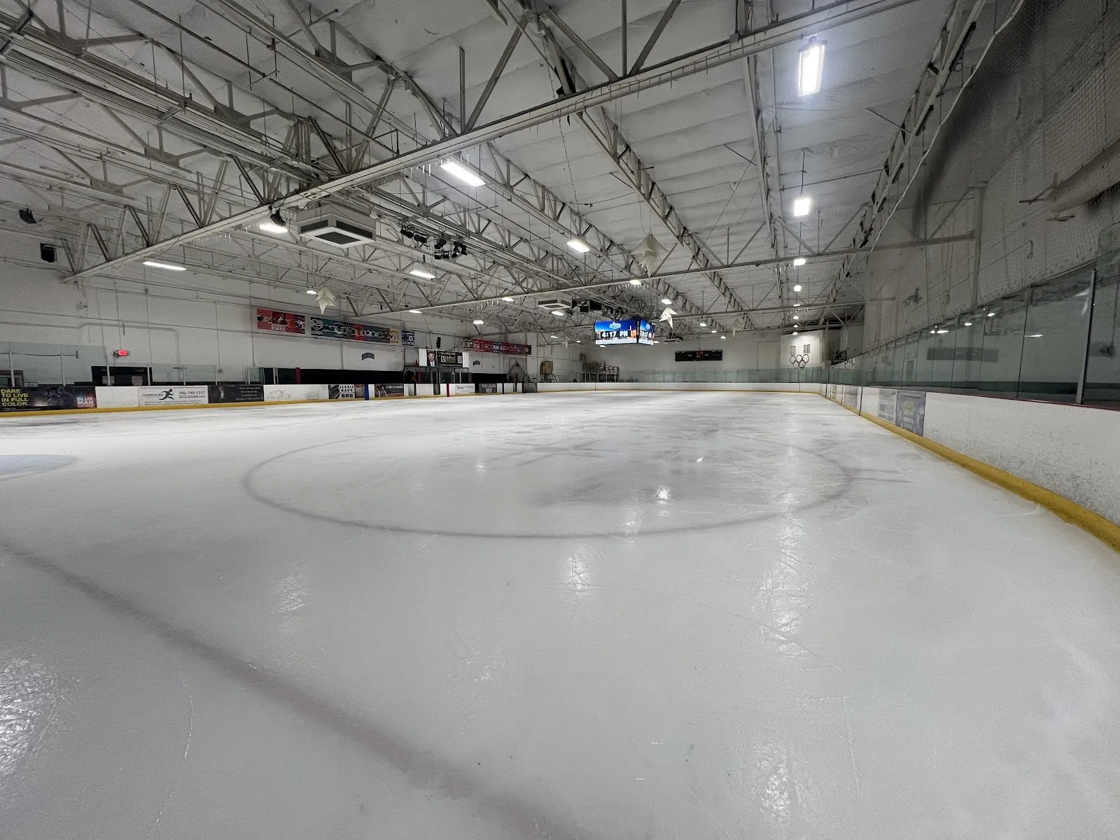 A long view along the boards of an empty sheet with a faint centre circle under a pale steel-trussed roof. — Las Vegas Ice Center