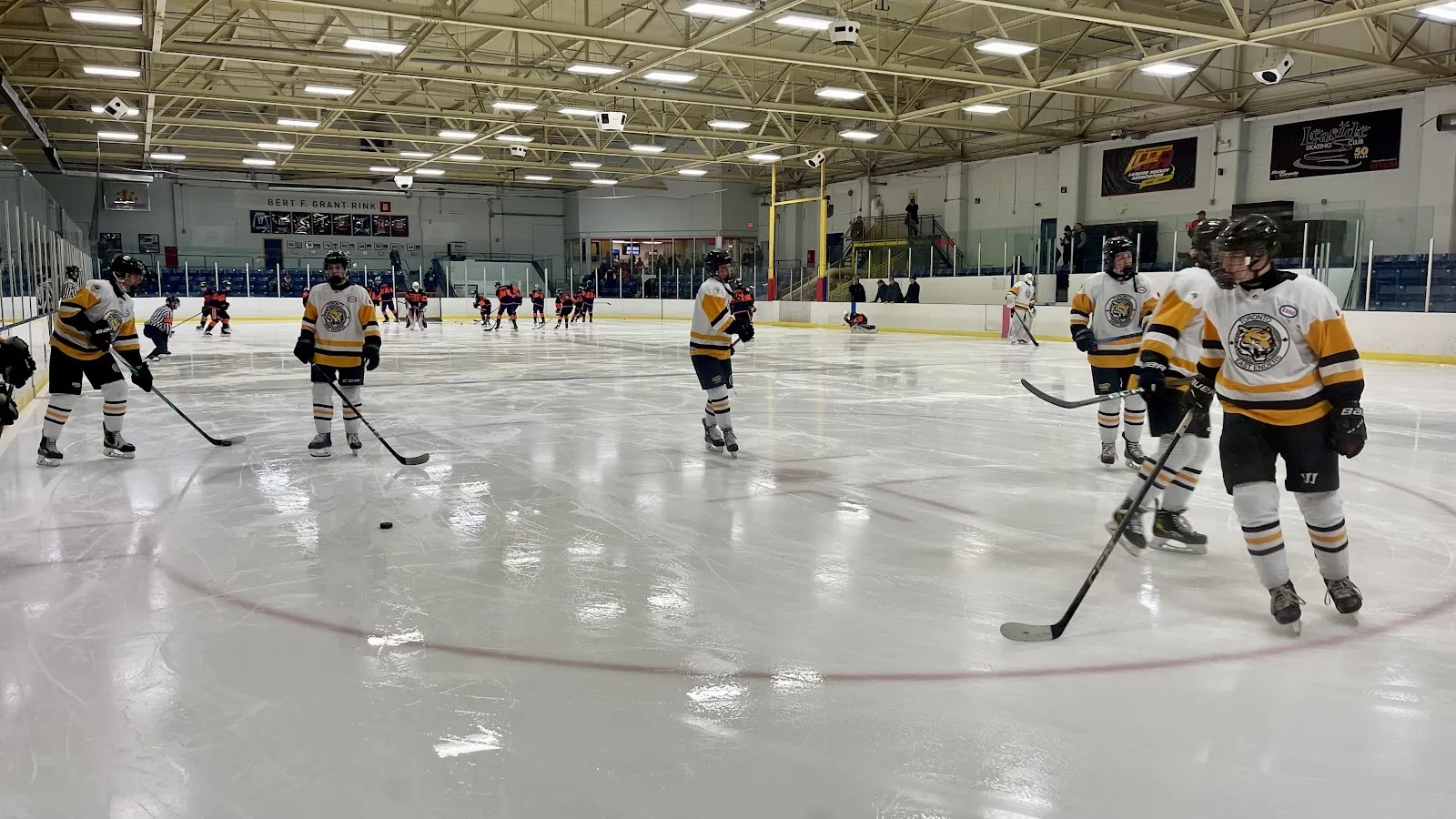 A game seen across the near corner, players spread across the sheet below a long wall of dark sponsor boards and red banners. — Leaside Memorial Community Gardens