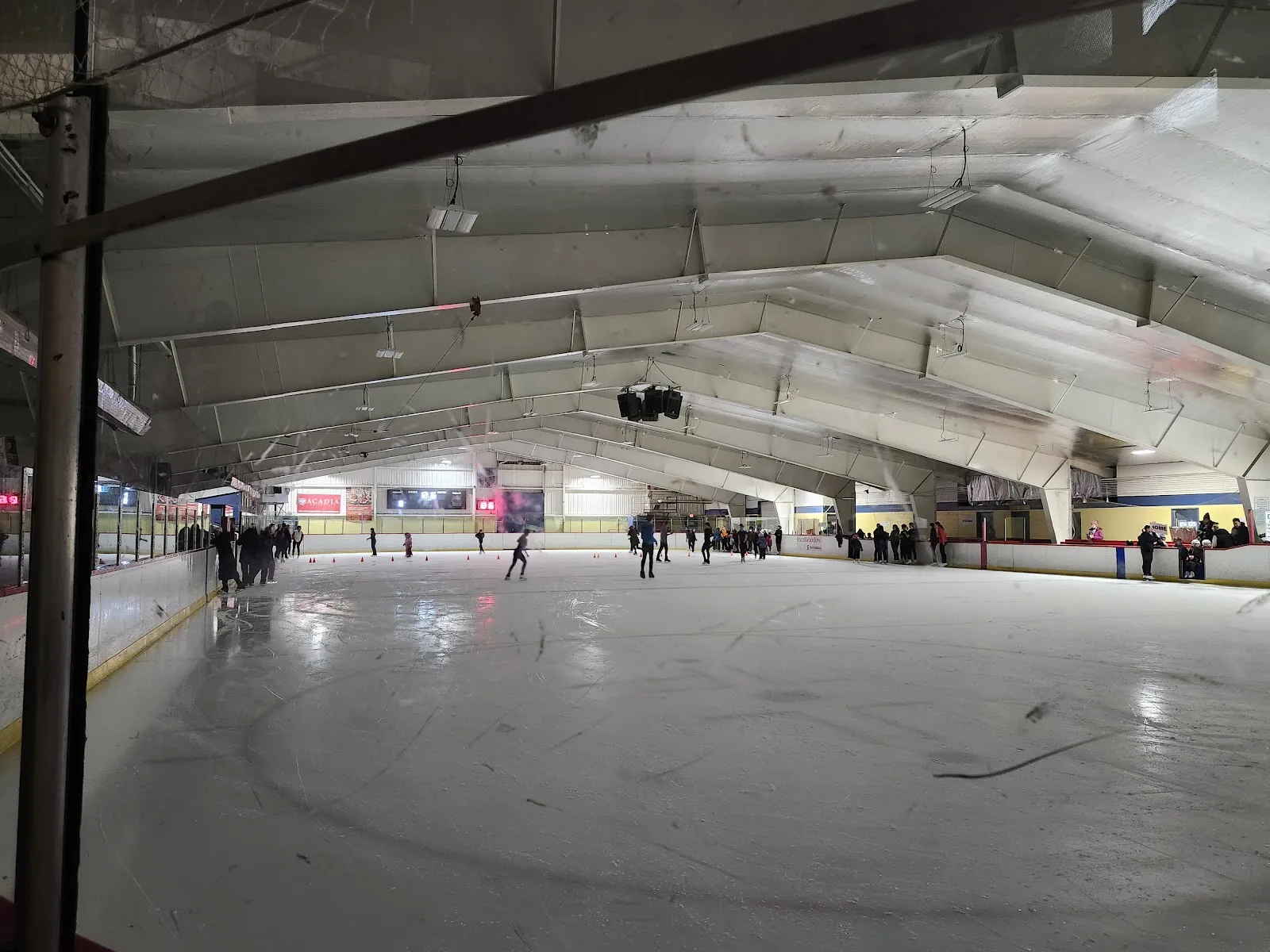 Skaters spread across the ice at LeBrun Arena in Bedford during a public skate, seen from the end of the sheet under the metal arch roof. — LeBrun Arena