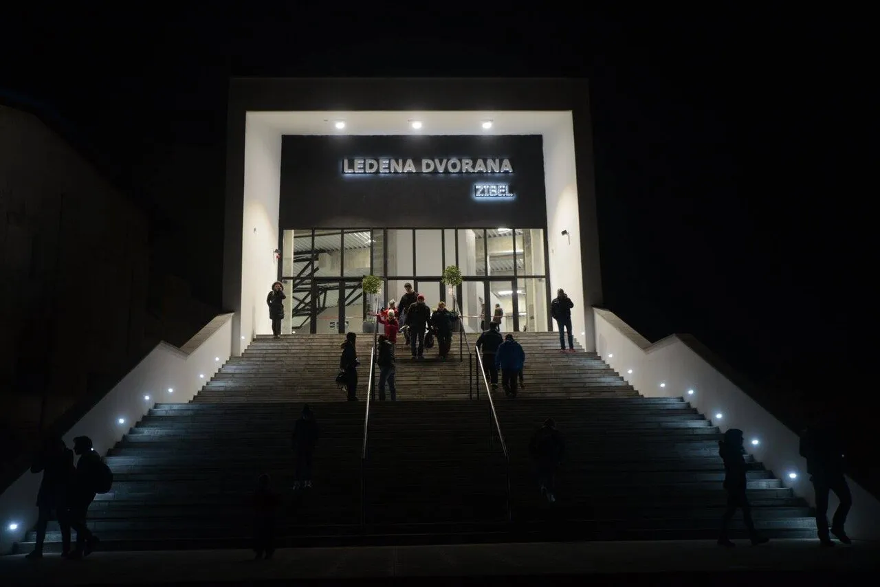 Stakleni ulaz Ledene dvorane Zibel noću, s osvijetljenim natpisom dvorane iznad širokih stuba. — Ledena dvorana Zibel Sisak