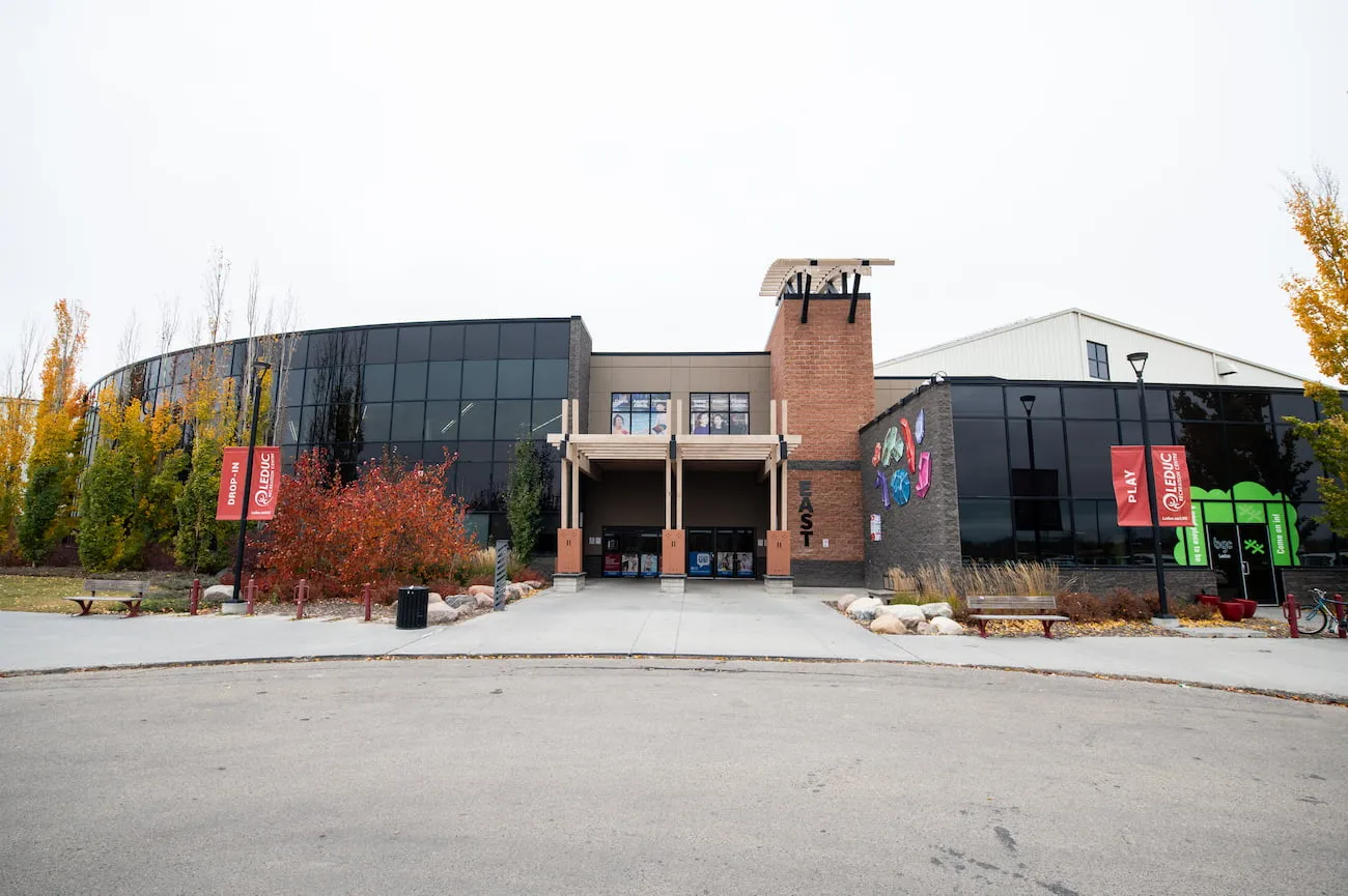 The Leduc Recreation Centre's east entrance: a brick tower and canopy between curved glass walls, with banners along the walk. — Leduc Recreation Centre