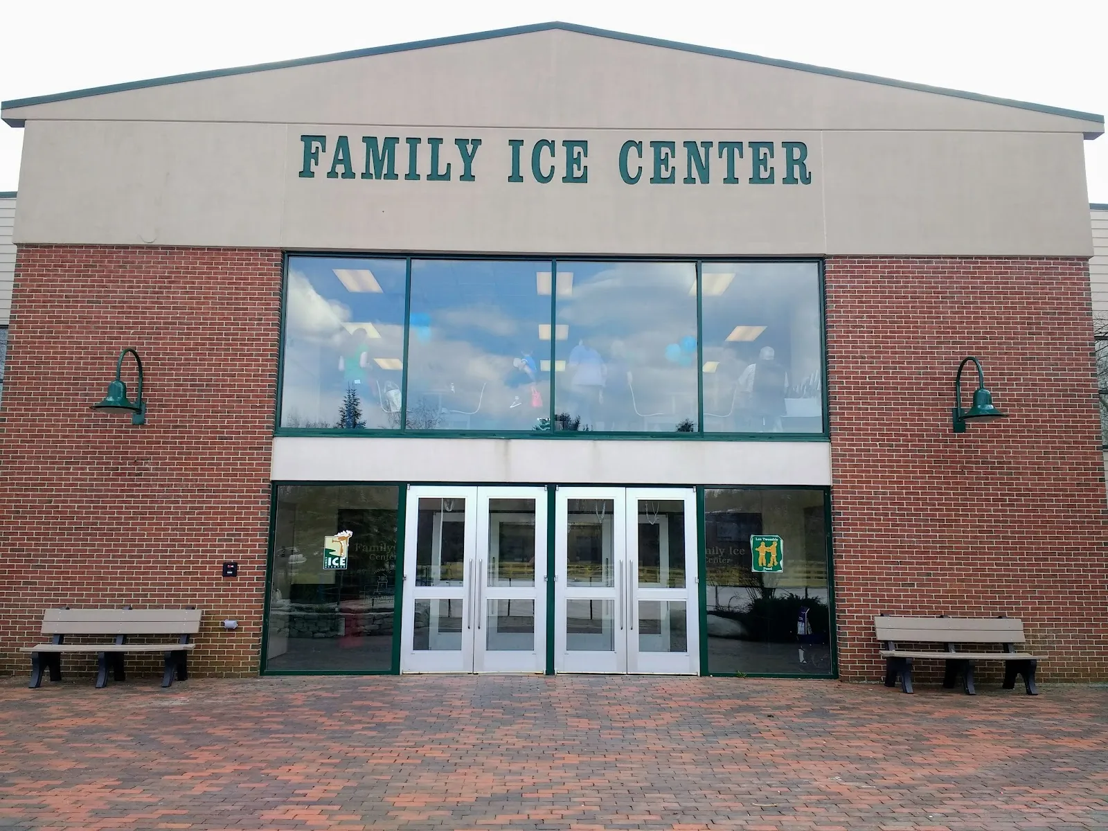 La entrada de ladrillo del Family Ice Center, casa del Lee Twombly Pond, con su nombre en el frontón sobre puertas de vidrio y bancas. — Lee Twombly Pond (Family Ice Center)