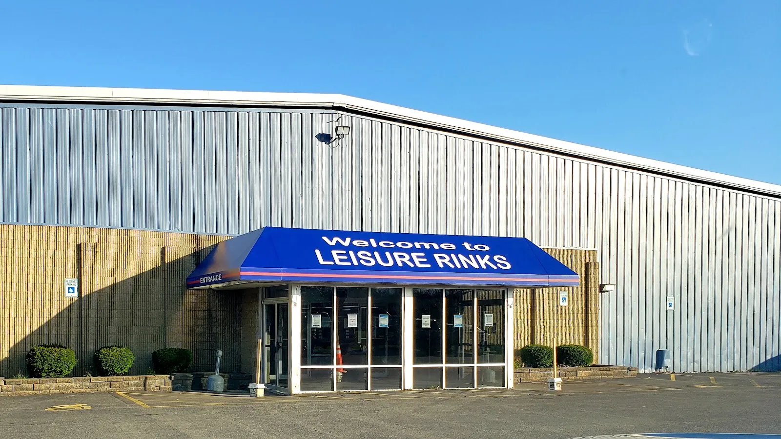 The Leisure Rinks entrance under a blue Welcome to LEISURE RINKS awning, set into a tall grey metal-sided rink building. — Leisure Rinks