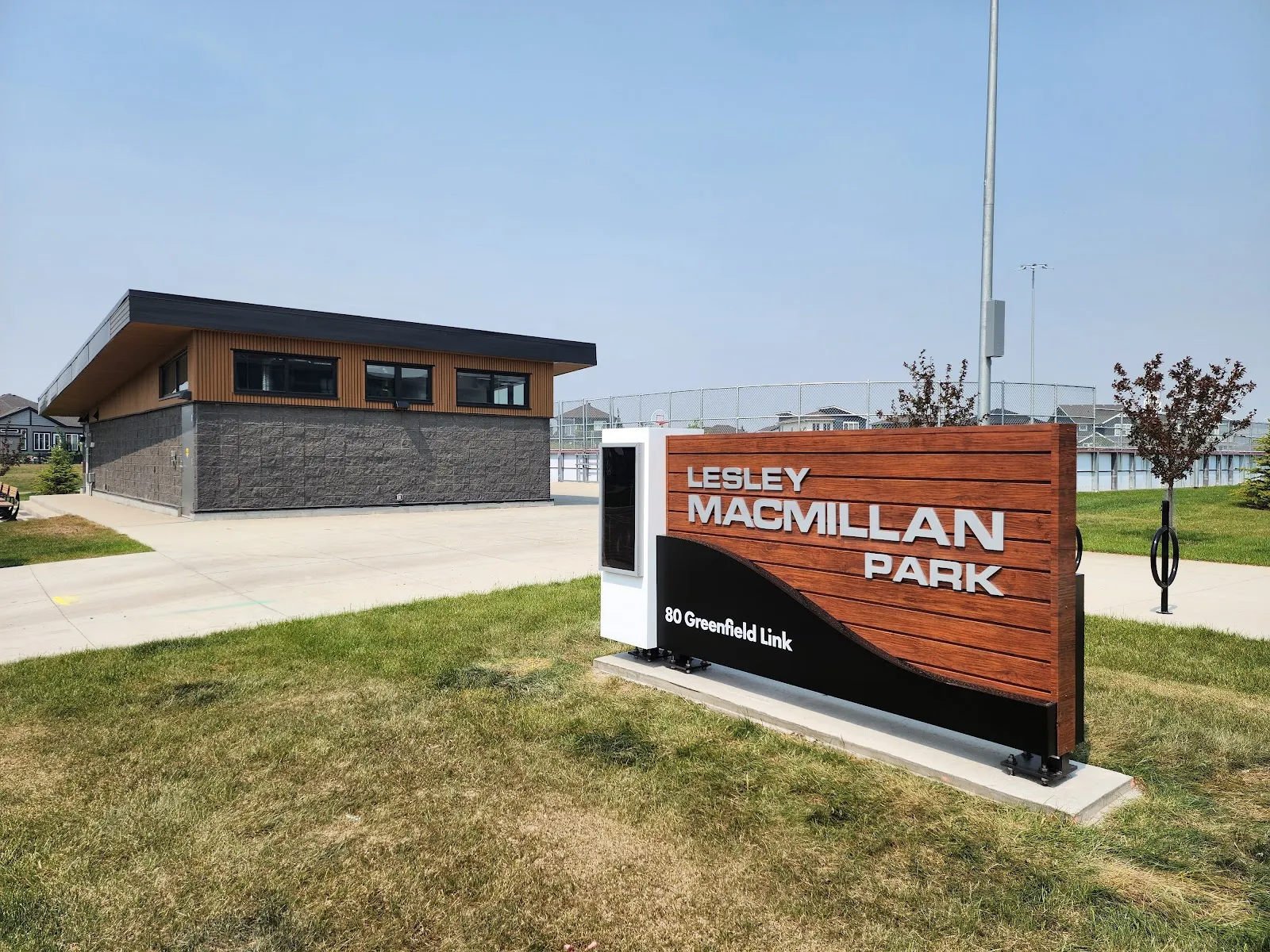 El edificio de calentamiento y el letrero del parque en Lesley Macmillan Park, en Fort Saskatchewan, junto a las vallas cercadas de la pista al aire libre — Lesley Macmillan Park Outdoor Rink