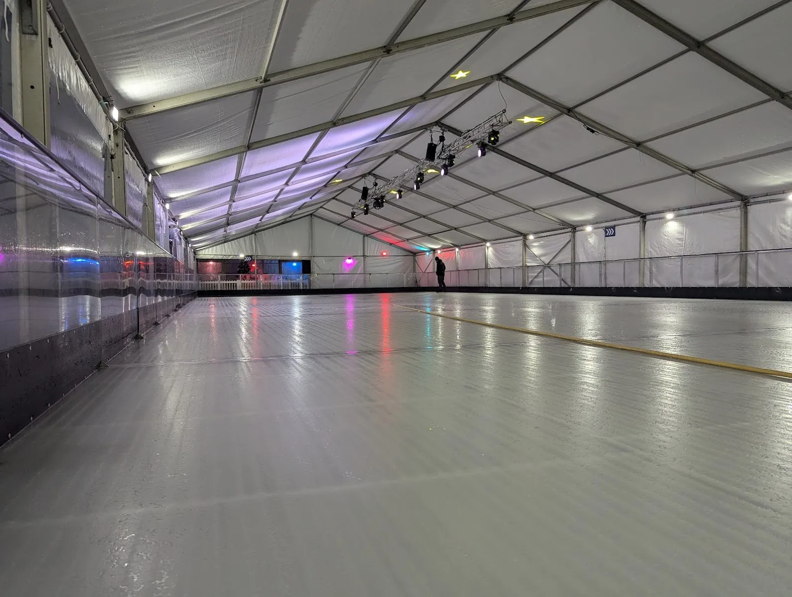 The empty ice sheet inside the long marquee at Letchworth Lido, with coloured lights and stage lighting above the boards — Letchworth Lido Ice Rink