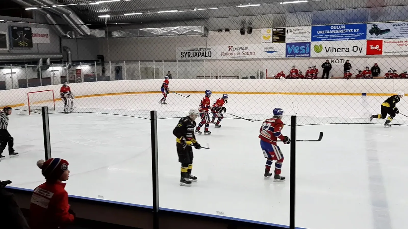 A hockey game on the Liminka hall's ice, seen through the boards netting – Limingan Jäähalli