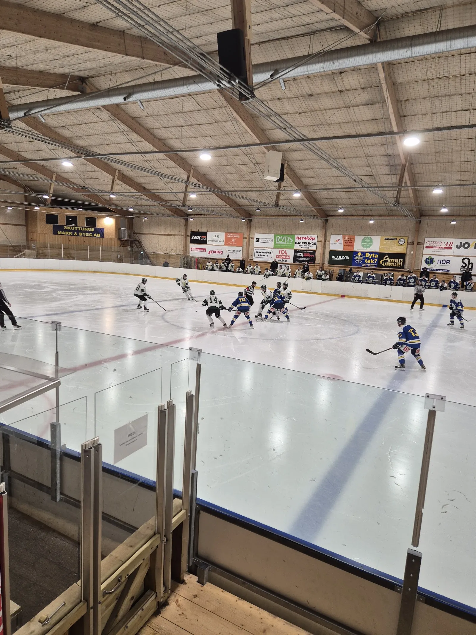 En ungdomsmatch i ishockey på isen i Lindbergs arena sedd från sargen under taket av trä – Lindbergs arena