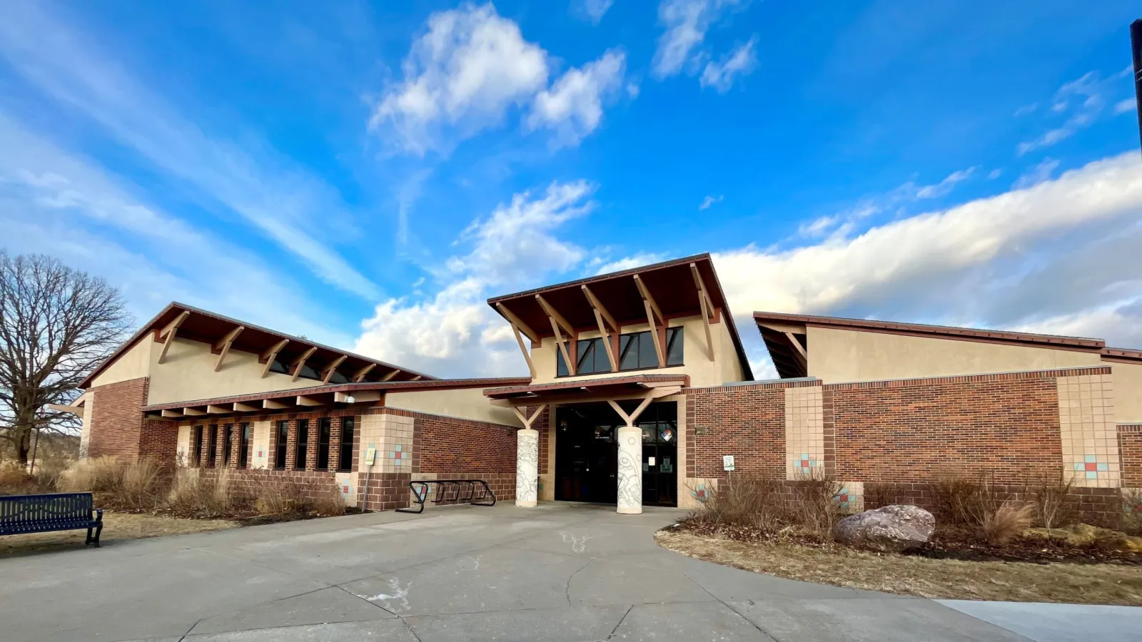 Front entrance of the Line Creek Community Center, a brick and stucco building with angled wood-beam roof overhangs, under a blue sky — Line Creek Community Center and Ice Arena