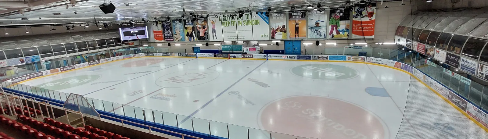The empty rink seen from the red spectator seats, with the Wildcats logo at centre ice, the scoreboard and banners along the far wall. — Link Centre