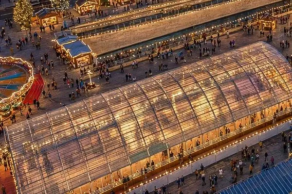 Aerial view of the glass-roofed Christmas Wonderland ice rink at Pier Head in Liverpool, with skaters on the ice and market stalls and crowds around it. — Liverpool Christmas Wonderland Ice Rink