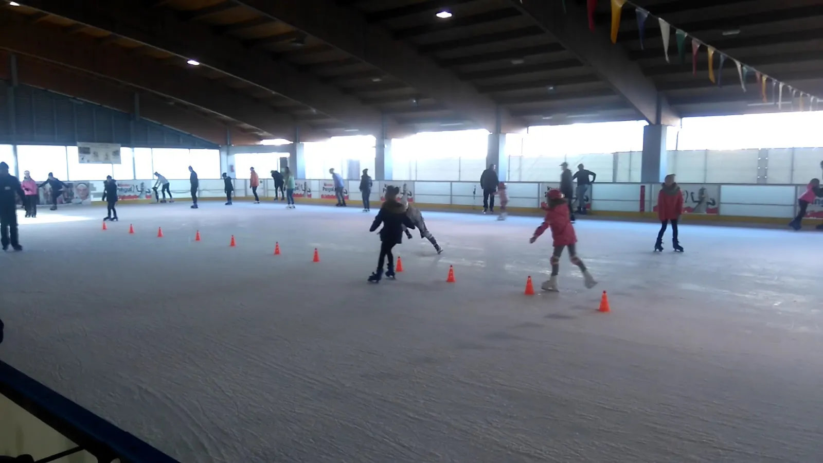 Skaters on the covered ice rink with slalom cones, seen from the boards — Lodowisko Aquapark Kalisz