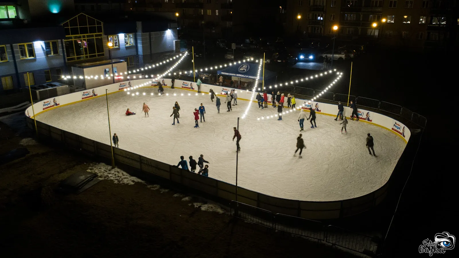 The lit open-air CSiR ice rink seen from above, with skaters — Lodowisko CSiR Augustów