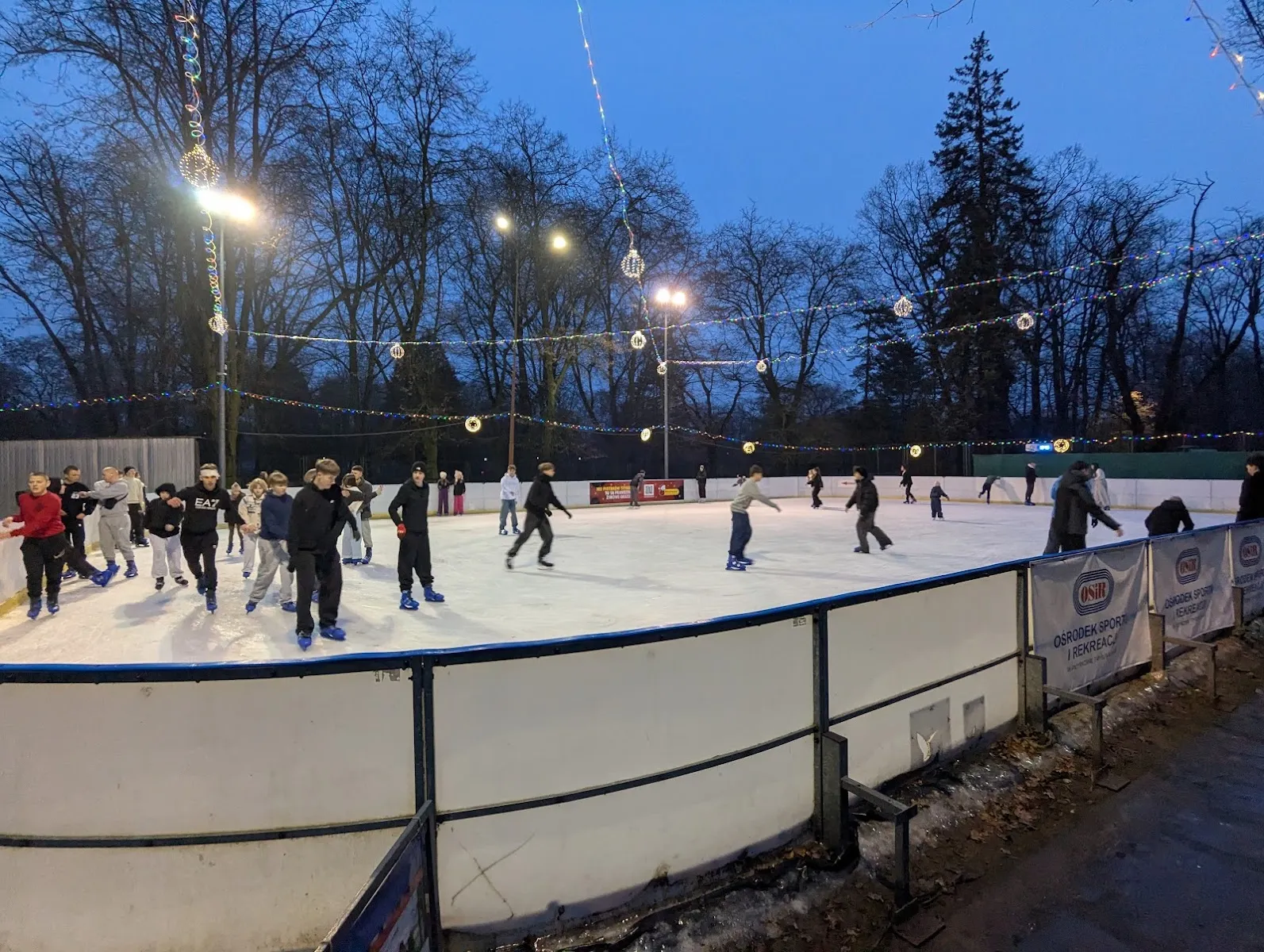 Skaters on the lit outdoor rink in the evening at the Piotrków Trybunalski municipal rink, with festive lights over the ice — Lodowisko Miejskie OSiR Piotrków Trybunalski
