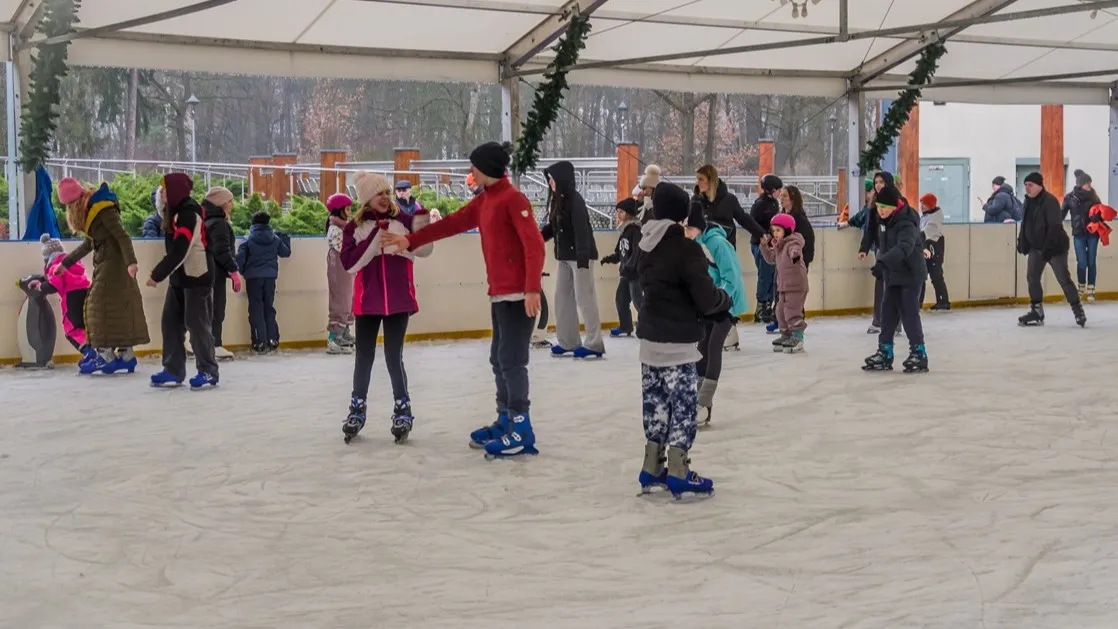 Skaters and children on the Konstancin-Jeziorna town rink under a festive canopy decorated with garlands. — Lodowisko miejskie w Parku Zdrojowym (Konstancin-Jeziorna)