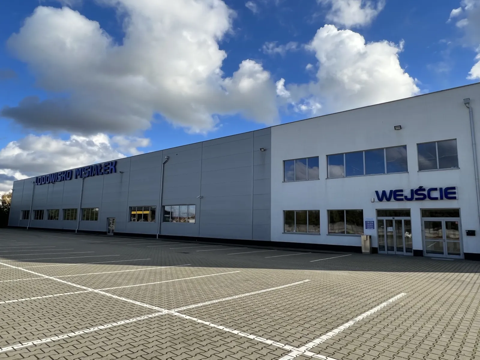 The grey building with its LODOWISKO MISIAŁEK sign and the WEJŚCIE entrance, with the car park in front. — Lodowisko Misiałek