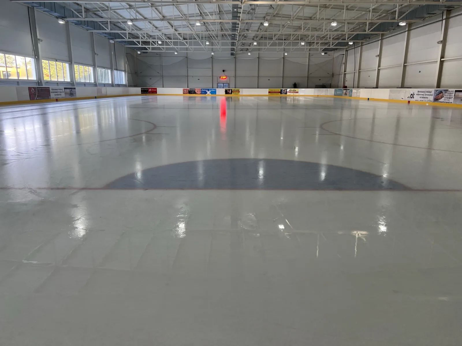 The ice surface of the covered hall, empty, with the dasher boards and the centre circle. — Lodowisko Misiałek