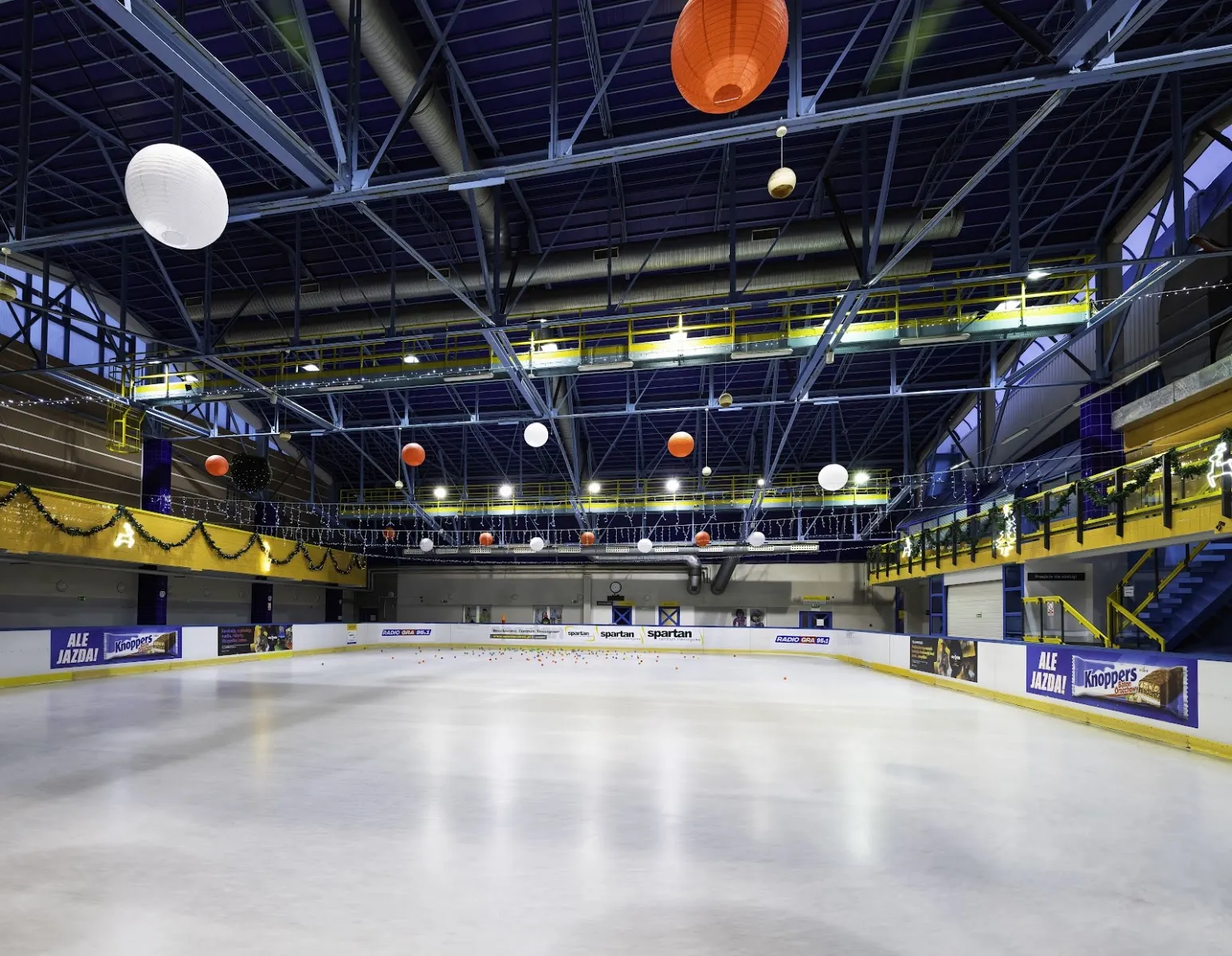 Empty ice sheet in the Orbita hall with white boards, hanging paper lanterns and the steel roof structure. — Lodowisko Orbita (WCT Spartan)