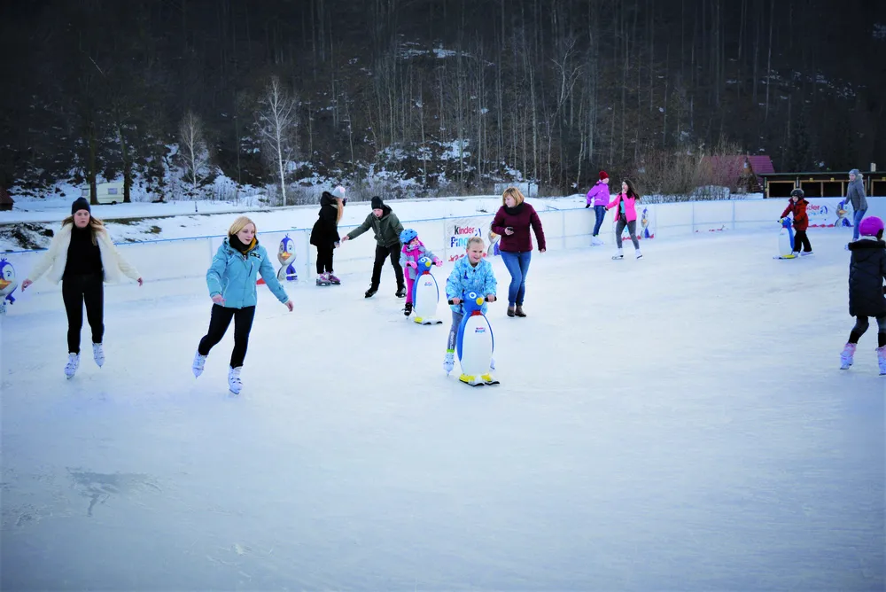 Skaters of all ages on the ice at the Brenna Park Turystyki rink, with some children using penguin skating aids. — Lodowisko w Parku Turystyki (Brenna)