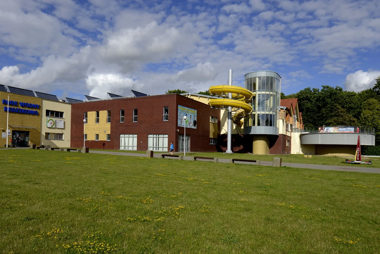The Strefa 360 Park building in Redzikowo that houses the covered ice rink, seen across the lawn from the path — Lodowisko Strefa 360 Park Redzikowo