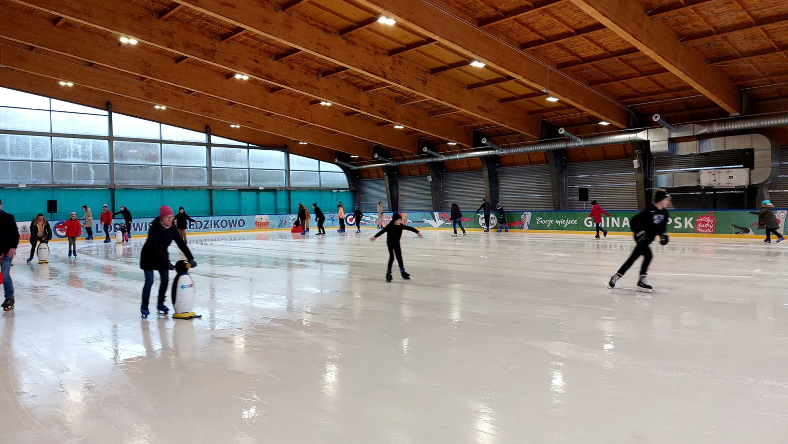 Skaters spread across the ice of the covered Redzikowo rink in the Strefa 360 park, under the timber roof — Lodowisko Strefa 360 Park Redzikowo
