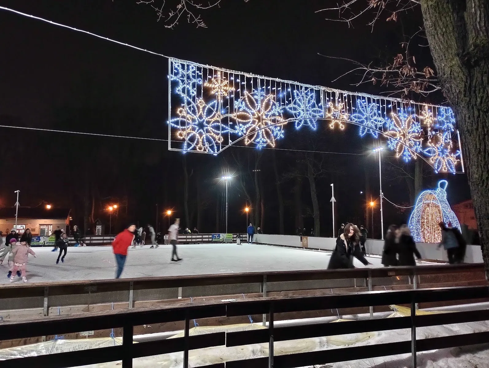 The seasonal ice rink in Grudziądz's city park at night with its festive lighting and skaters at a distance — Lodowisko Sezonowe w Parku Miejskim Grudziądz