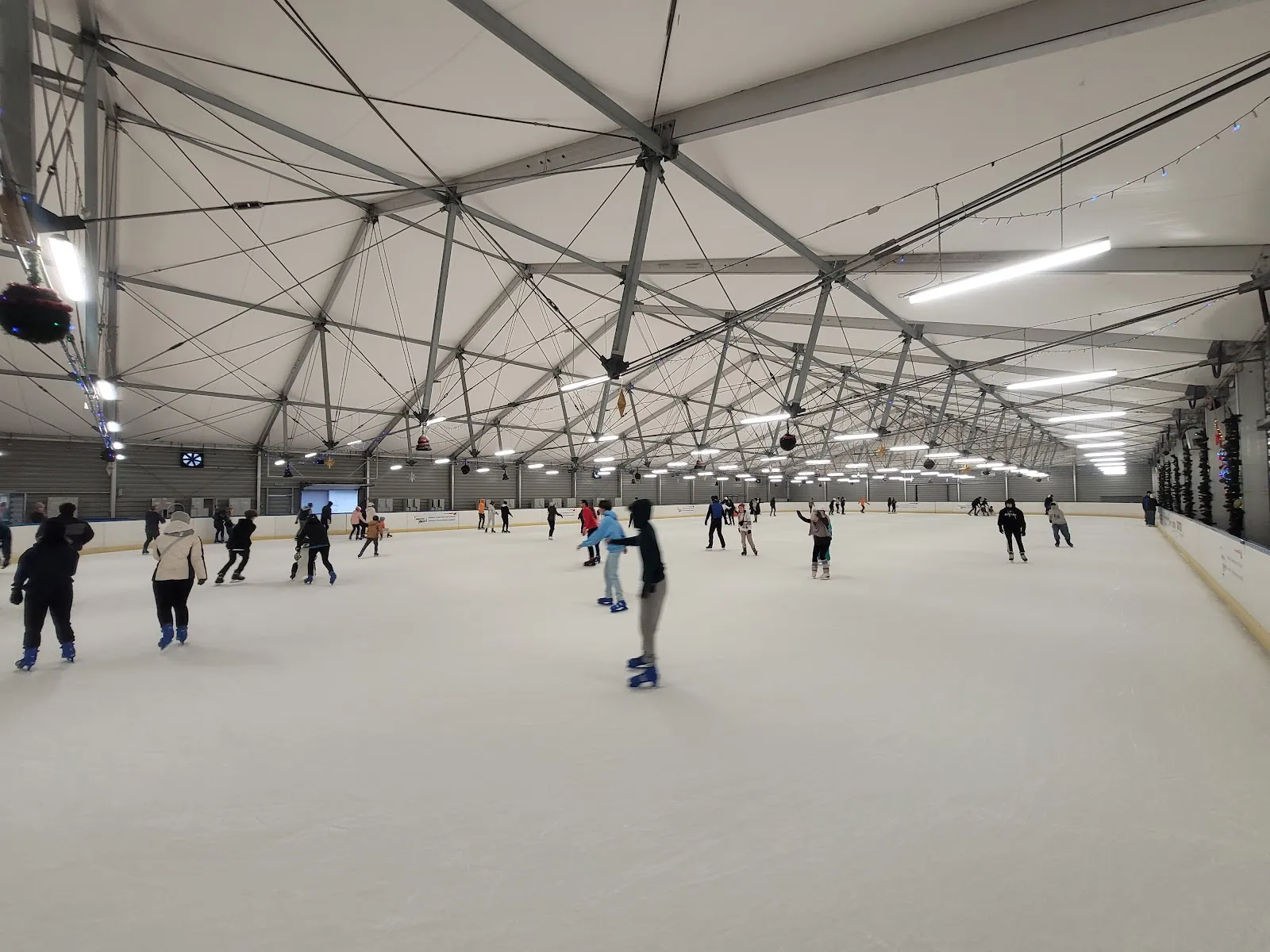 Wide view across the covered Spiska ice under the white tension-roof hall, with skaters spread far apart. — Lodowisko Spiska (WCT Spartan)
