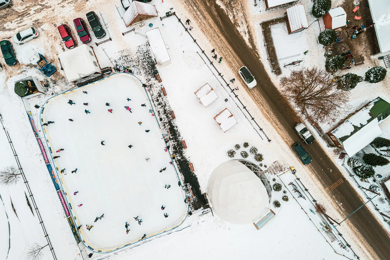 Aerial view of the Bałtów rink beside the white dome, with skaters on the ice and the resort buildings around it — Lodowisko Szwajcaria Bałtowska
