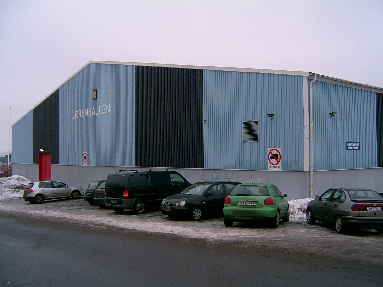 The Løren ishall in Oslo seen from the car park: a long hall clad in blue and black panels. — Løren ishall