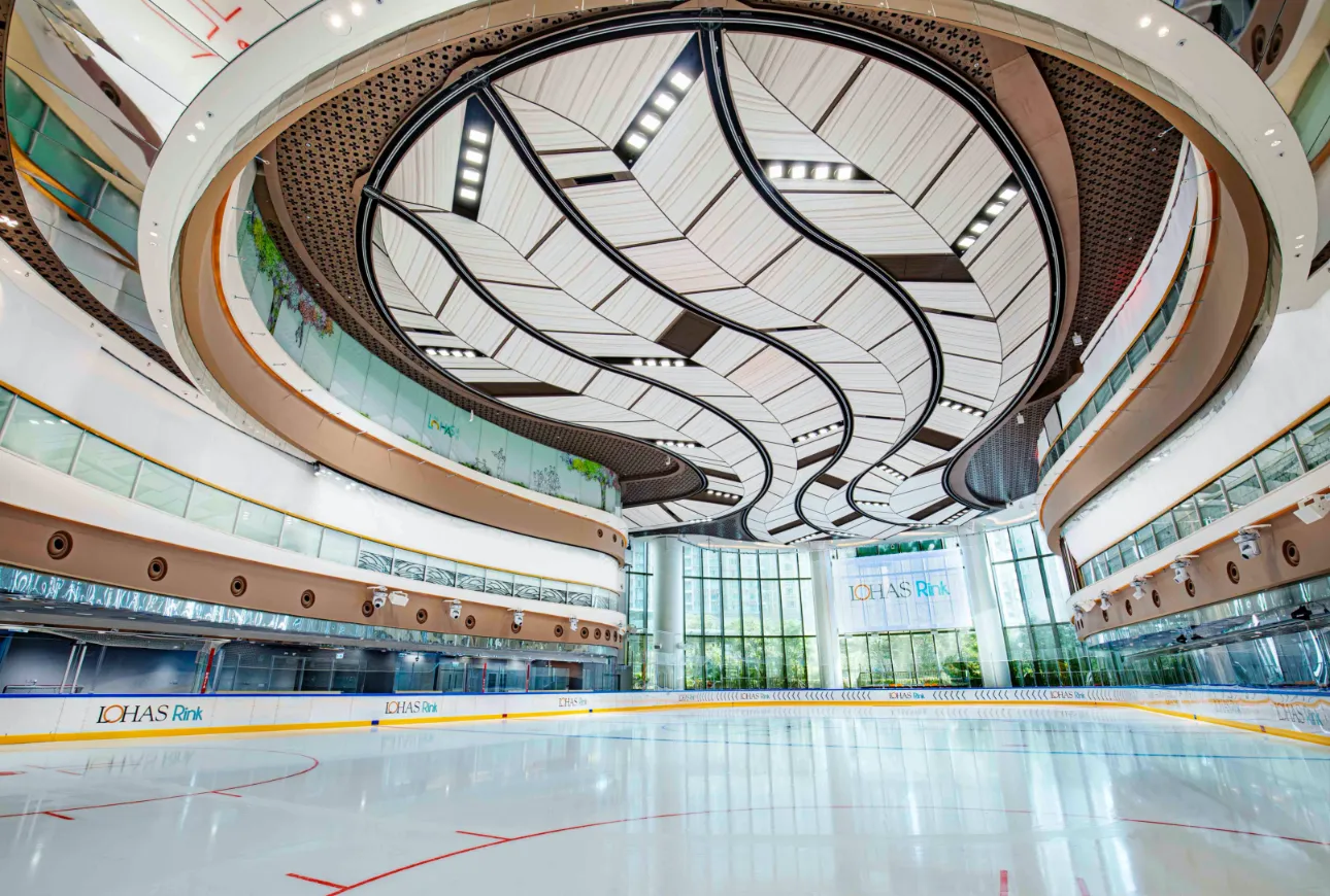 康城內彎曲白色天花板下空無一人的 LOHAS Rink 冰面，旁邊是圍板和場邊座位（溜冰場自己網站上發布的照片）。 — LOHAS Rink