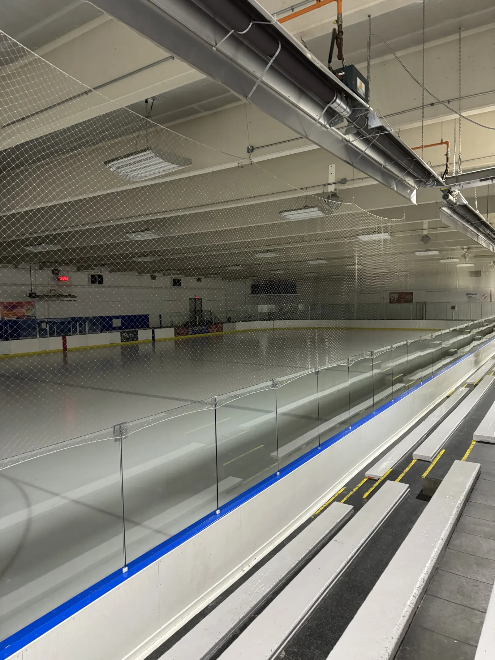 El hielo vacío visto a lo largo del cristal desde las gradas, con vallas de borde azul y red bajo un techo blanco. — Londonderry Arena