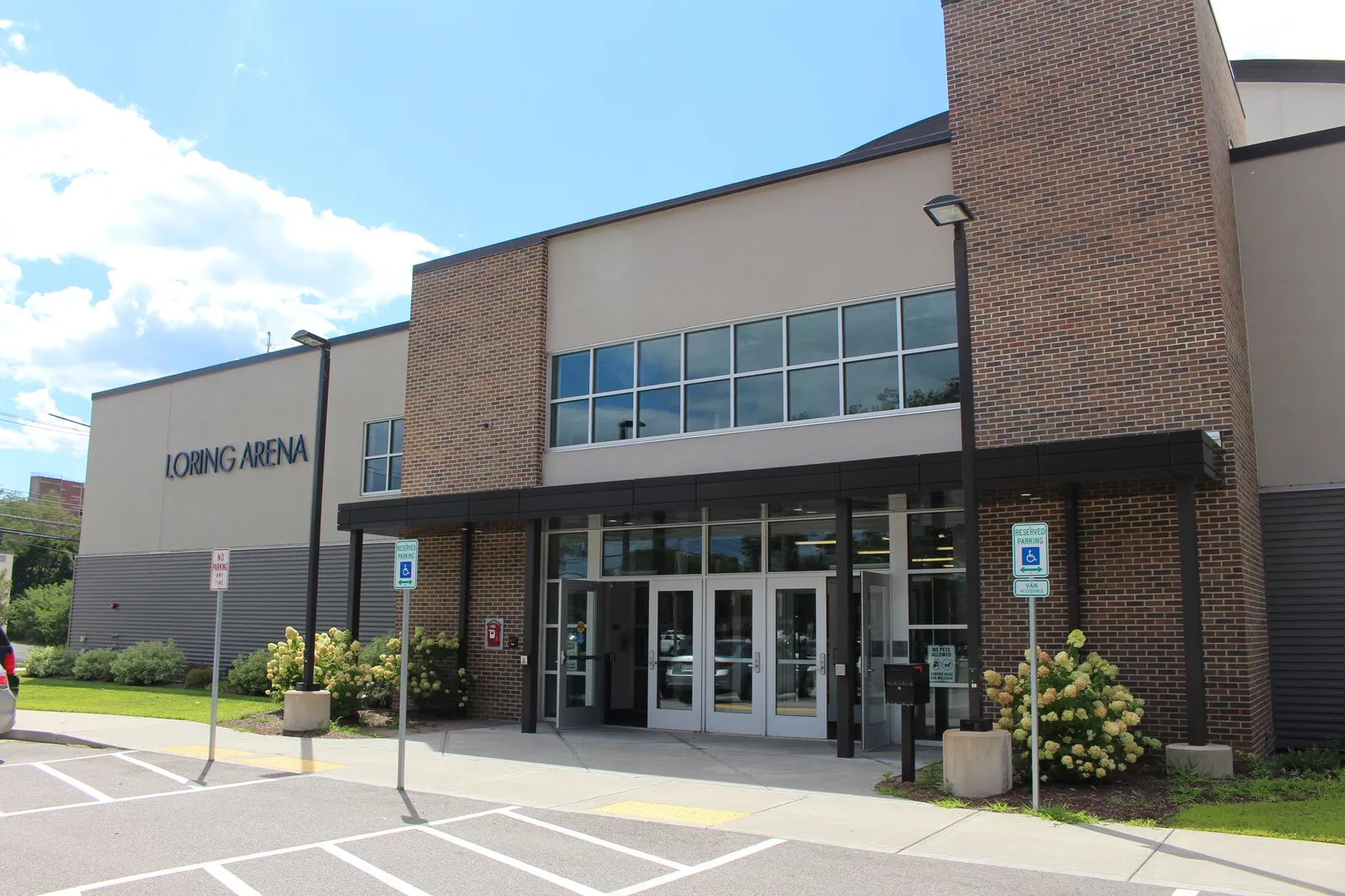 The brick and glass entrance of Loring Arena in Framingham, with its name above the doors and accessible parking in front. — Loring Arena
