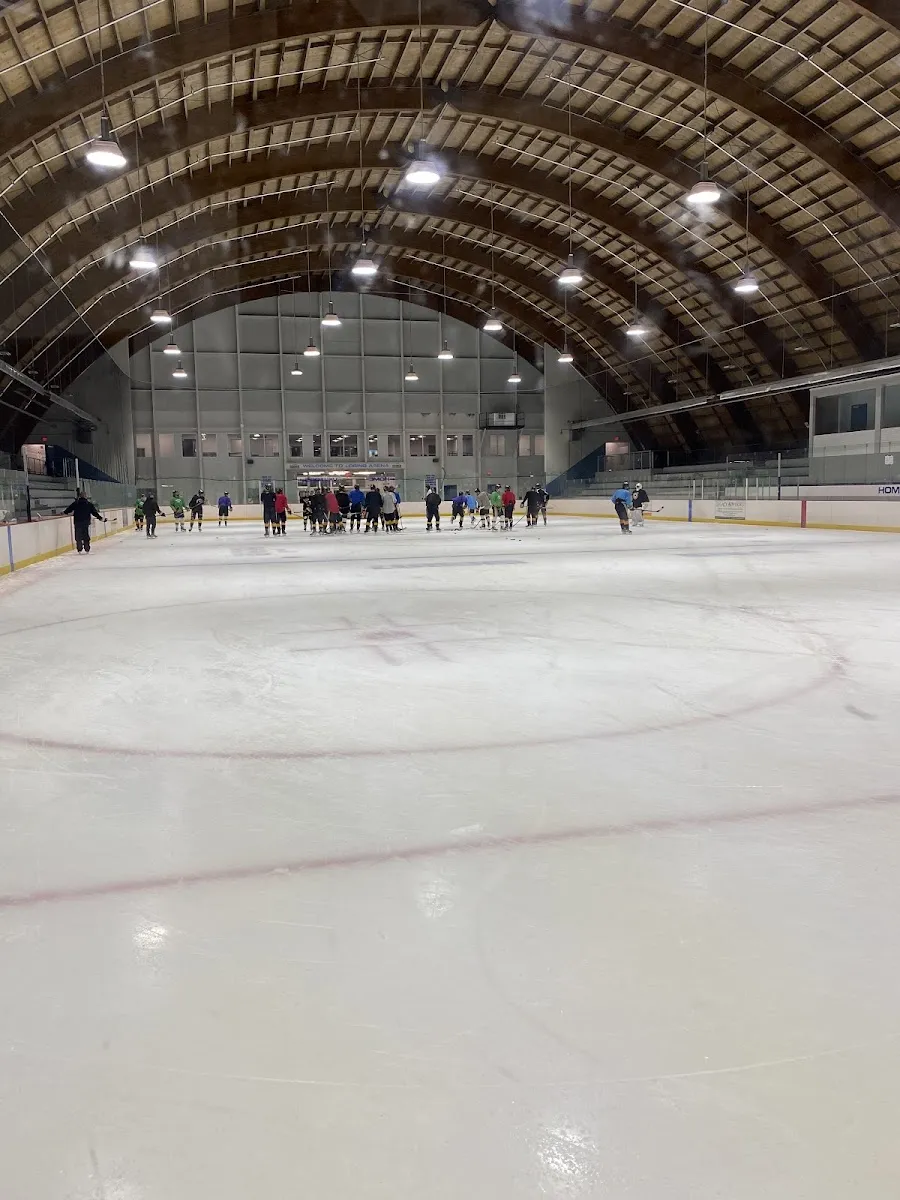 The ice under the arena's arched wooden barrel roof, with a group of skaters gathered at the far end in front of the end wall. — Loring Arena