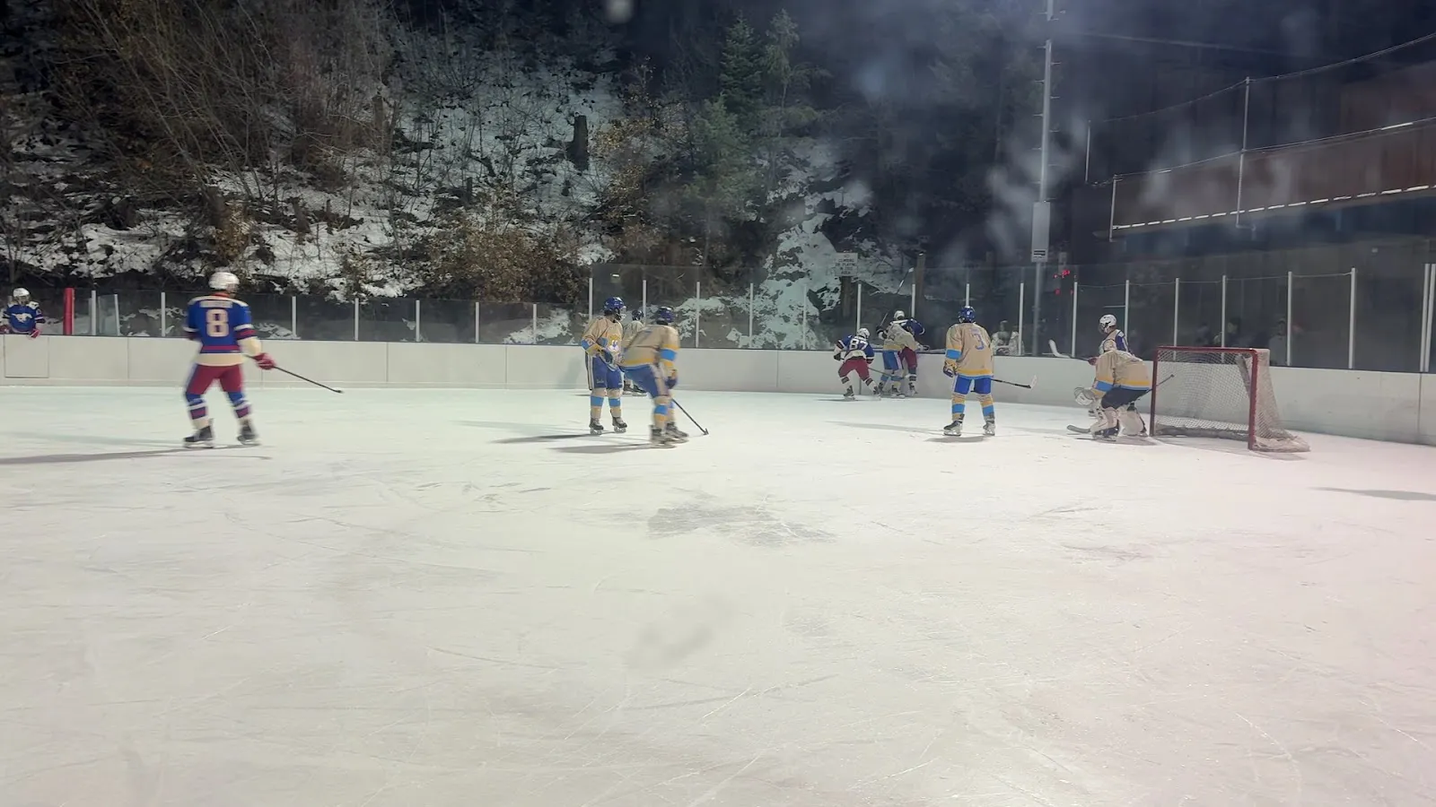 An evening hockey game on the floodlit Los Alamos rink with players spread across the ice. — Los Alamos County Ice Rink