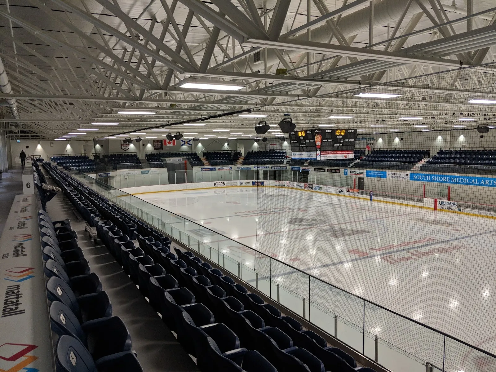La arena vista desde un asiento junto al vidrio, con una pista vacía y hileras de asientos azul oscuro curvándose alrededor bajo un techo de armaduras de acero. — Lunenburg County Lifestyle Centre