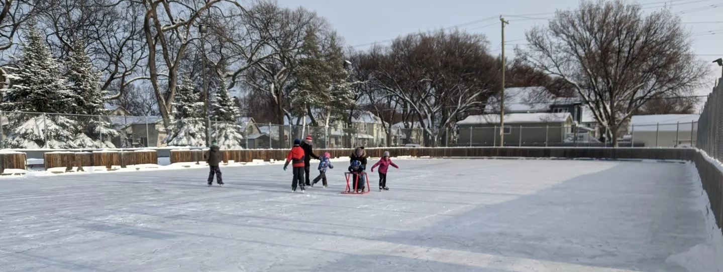The Luxton outdoor rink in winter with a few skaters on the ice and houses behind the boards — Luxton Community Centre Outdoor Rink