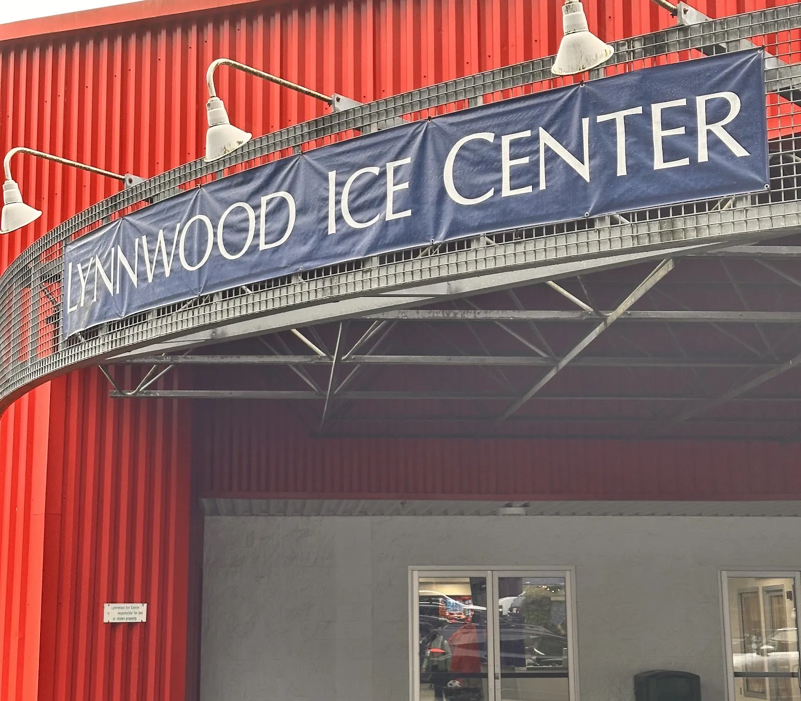 The Lynnwood Ice Center entrance: the name banner on a curved steel canopy over the doors, set into the red corrugated rink building — Lynnwood Ice Center
