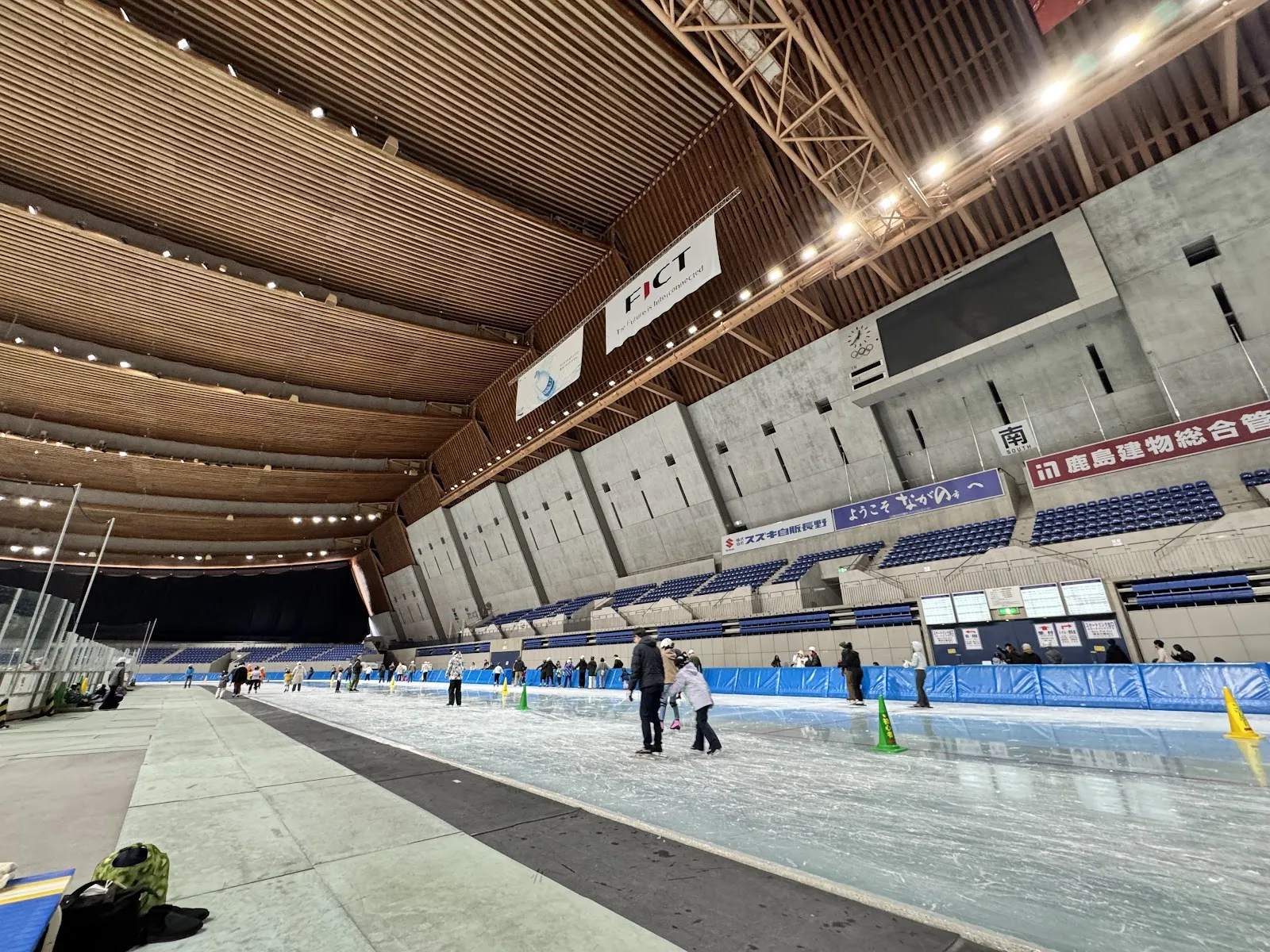 The 400 metre speed-skating oval of M-Wave seen along the track with its timber roof and concrete stands, with a few skaters at the far side — M-Wave (Nagano Olympic Memorial Arena)