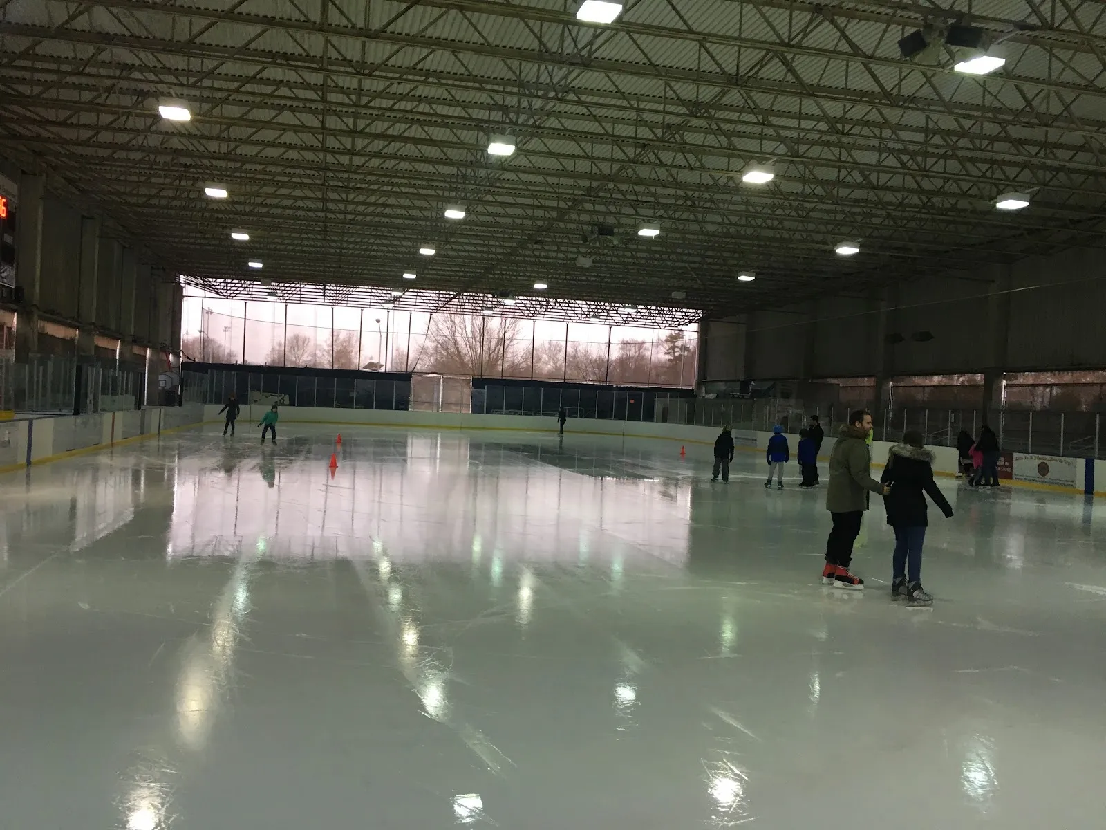 Una vista amplia de una sesión pública, con patinadores repartidos por una pista larga bajo un techo oscuro de armaduras de acero con un banderín al fondo. — Mackay Ice Rink