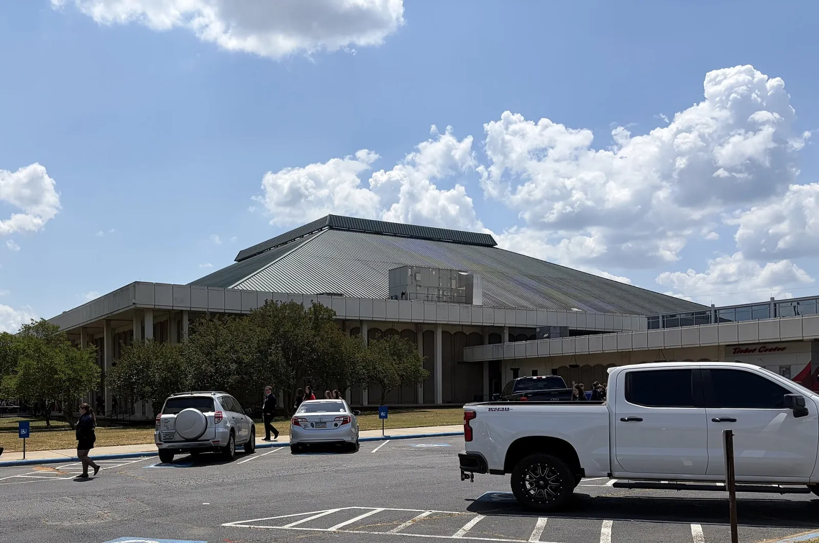 The Macon Coliseum seen from the parking lot, with its low concrete front, tree-lined walkway and large pitched metal roof — Macon Coliseum Public Skating