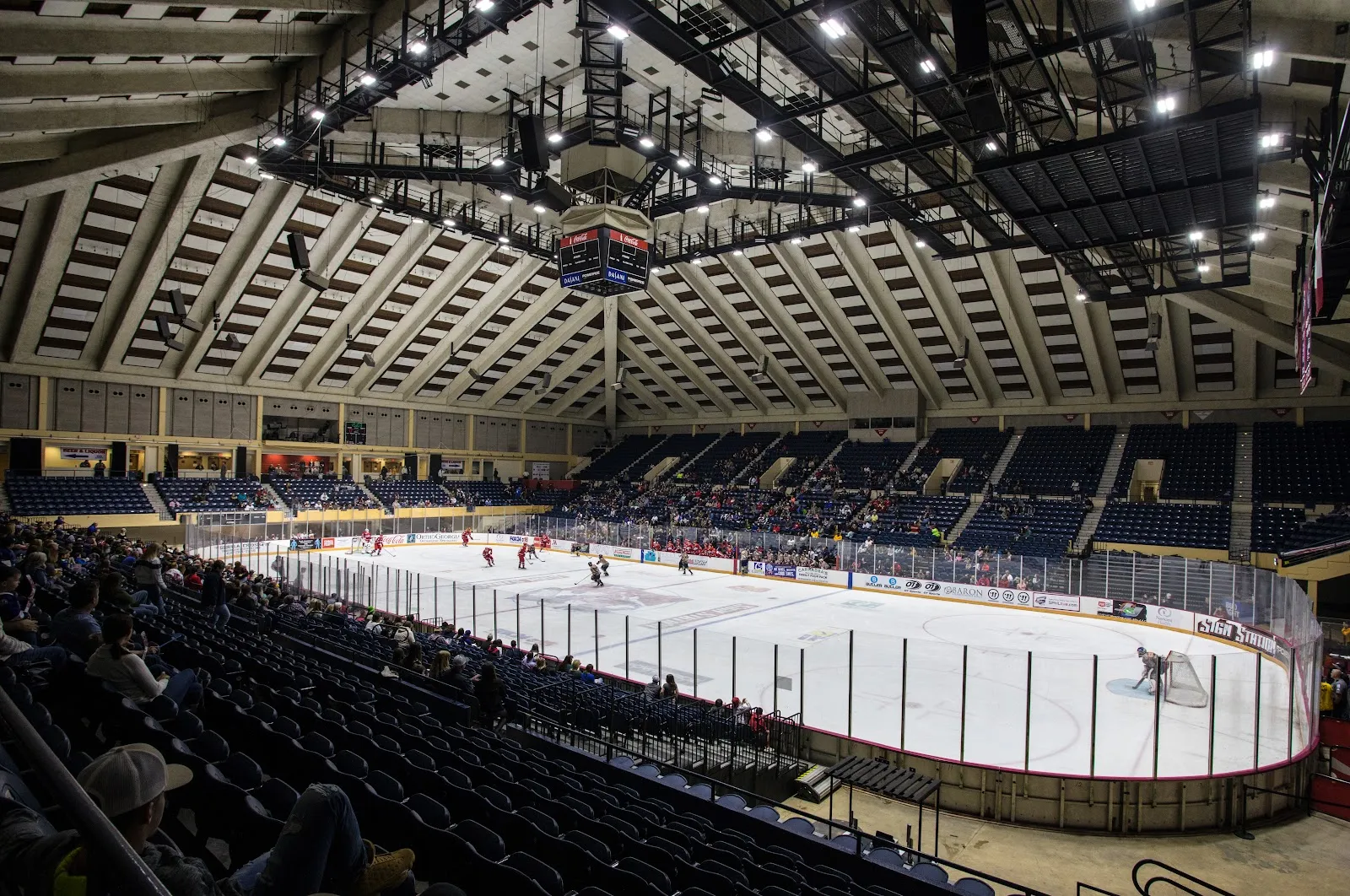 The Macon Coliseum arena with its ice sheet set up for a hockey game, a team playing at a distance, glass above the boards and the coffered roof over the stands. — Macon Coliseum Public Skating