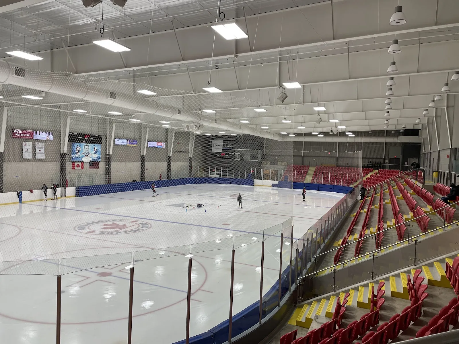 La pista principal desde la esquina, con asientos rojos y amarillos a lo largo de un costado y algunos patinadores en el hielo. — Magna Centre (Newmarket)