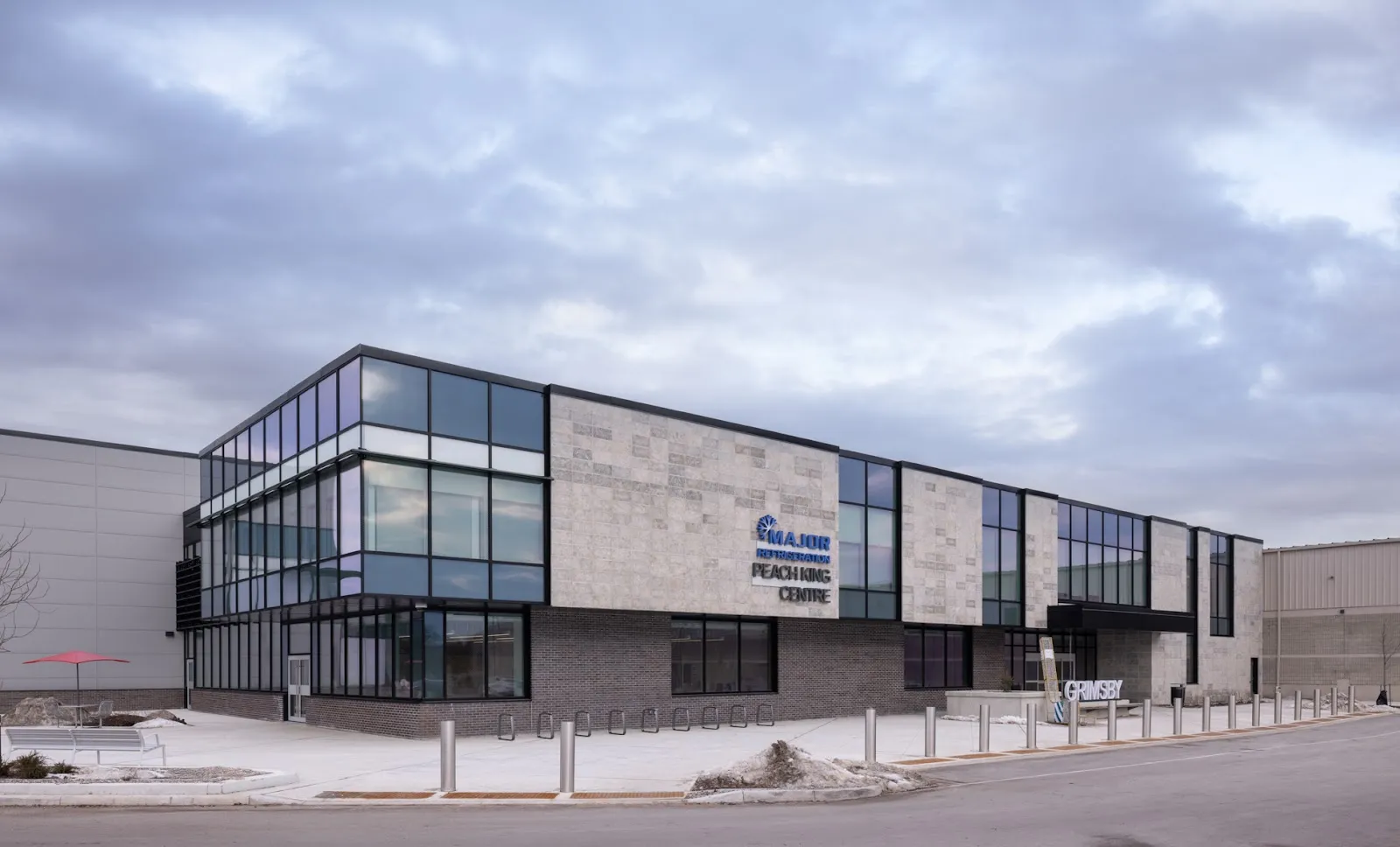 El edificio ampliado del Major Refrigeration Peach King Centre visto desde la calle, con su fachada de cristal y piedra y el nombre del centro en la pared. — Major Refrigeration Peach King Centre