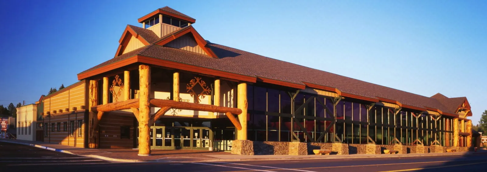 The log-and-glass exterior of Manchester Ice & Events Centre on East Lake Street, with a snowflake emblem over the entrance, lit by evening sun. — Manchester Ice & Events Centre